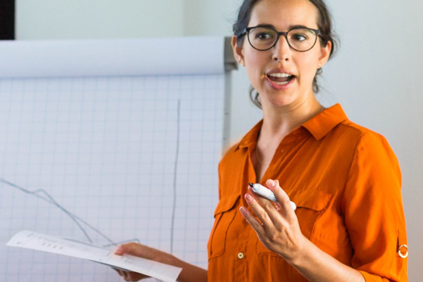 Frau in oranger Bluse erklärt an Whiteboard