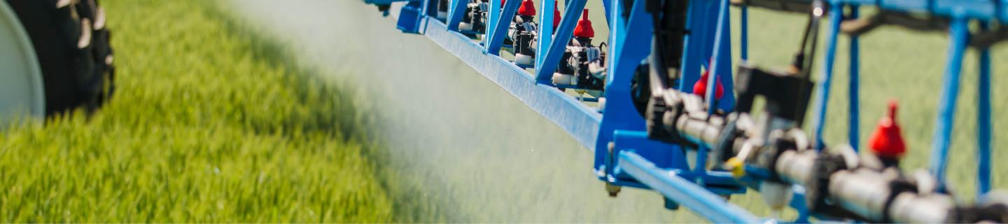 Grünes Getreidefeld mit blauer Pflanzenschutzspritze in Behandlung.