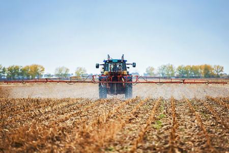 A tractor equipped with a sprayer moves across a vast field